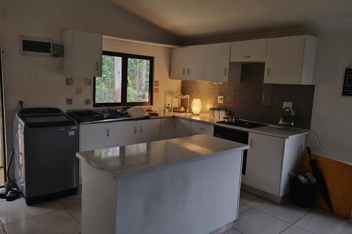 Functional kitchen featuring white cabinetry, a central island, tiled backsplash, and integrated cooking appliances with direct garden views.