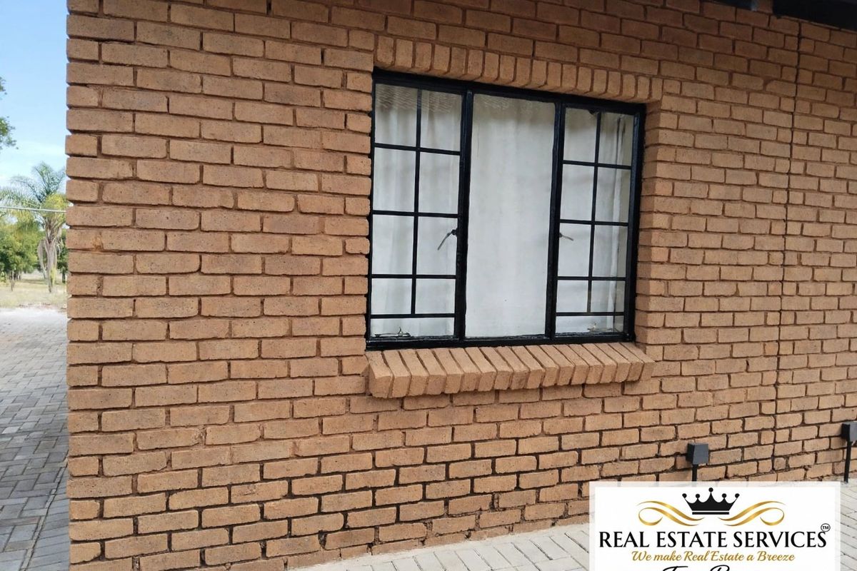 Exterior view of a face brick apartment wall featuring a black metal framed window with security bars and a paved walkway.