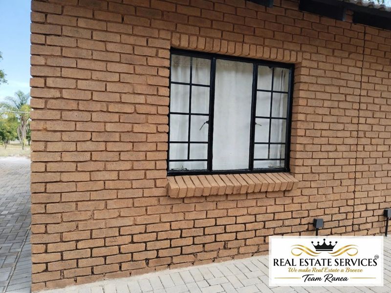 Exterior view of a face brick apartment wall featuring a black metal framed window with security bars and a paved walkway.