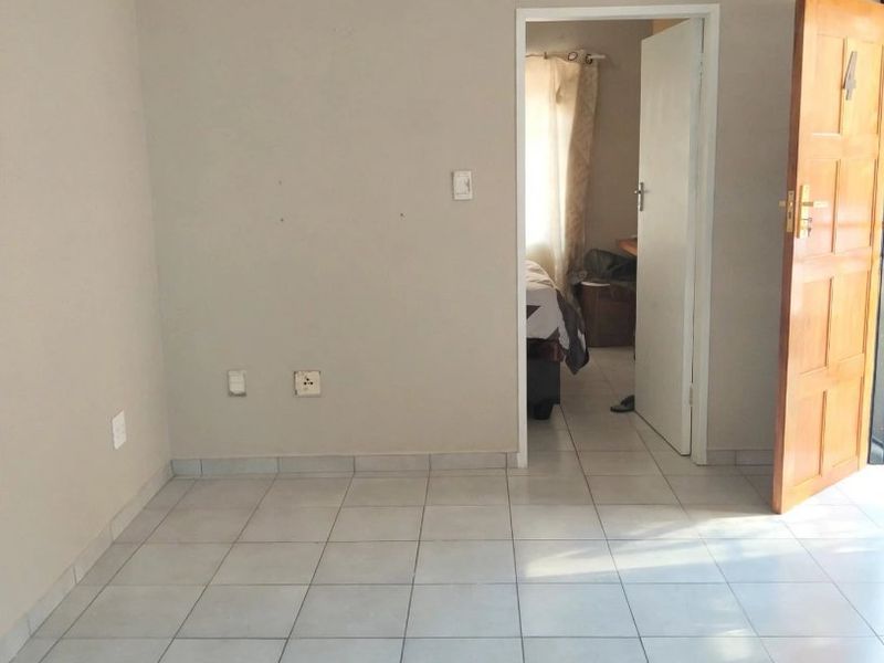 An empty bedroom featuring neutral wall paint, tiled flooring, and a wooden door leading to an adjacent room.