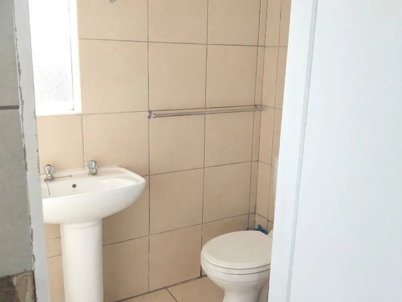 A compact bathroom featuring a pedestal basin, toilet, and neutral wall and floor tiling, offering a functional space ready for modernization.