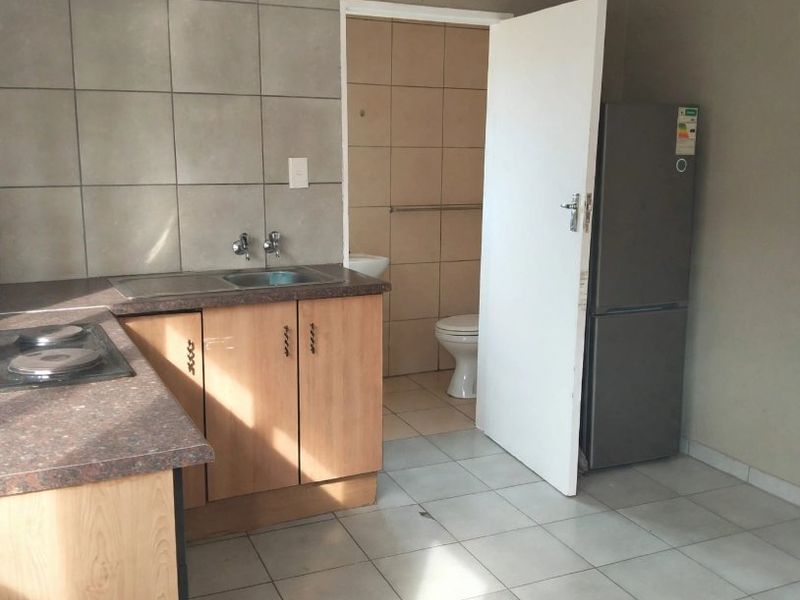 A functional kitchen area featuring built-in cabinetry, a laminate countertop, and a built-in hob, with direct access to an adjacent bathroom.