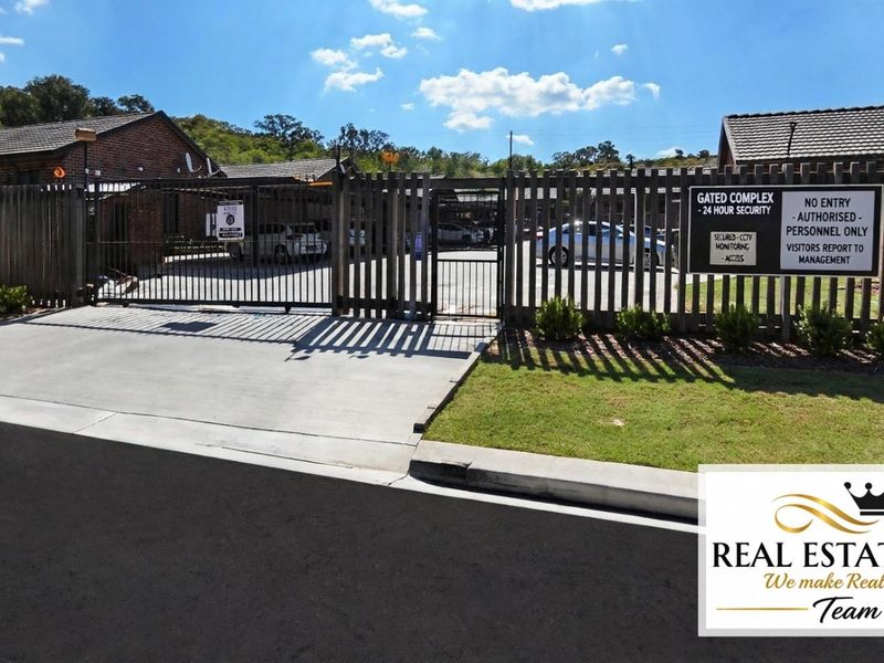 The entrance to the gated residential complex featuring secure perimeter fencing, a controlled access gate, and 24-hour security monitoring.