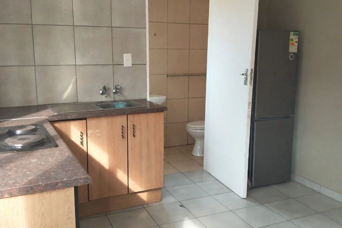A functional kitchen area featuring built-in cabinetry, a laminate countertop with a built-in hob, and tiled splashbacks, with direct access to an adjacent bathroom.