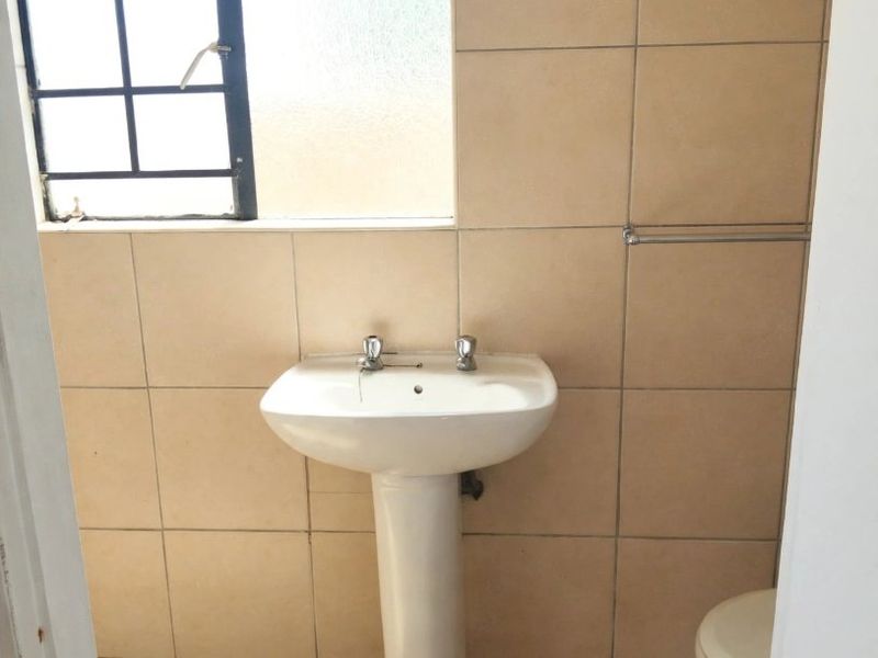 A compact bathroom featuring a pedestal basin, tiled walls and flooring, and a window with security bars.