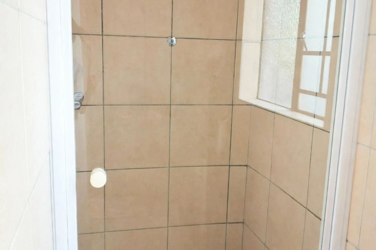 A functional shower stall featuring neutral wall and floor tiling, a glass enclosure, and a window for natural light.