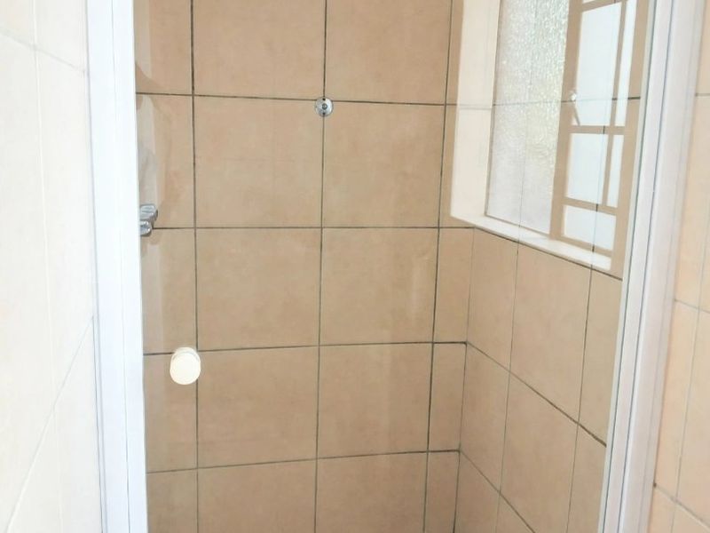 A functional shower stall featuring neutral wall and floor tiling, a glass enclosure, and a window for natural light.