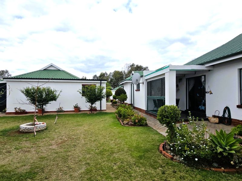 Rear view of the townhouse featuring a well-maintained lawn, paved patio area, and established garden beds with brick edging.