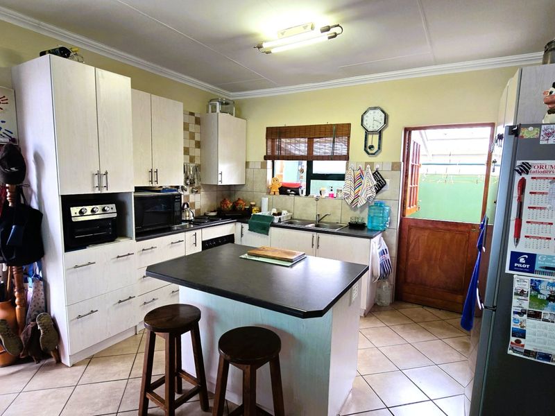 A functional kitchen featuring light-toned cabinetry, a central island with a dark countertop, tiled flooring, and direct access to an outdoor area.