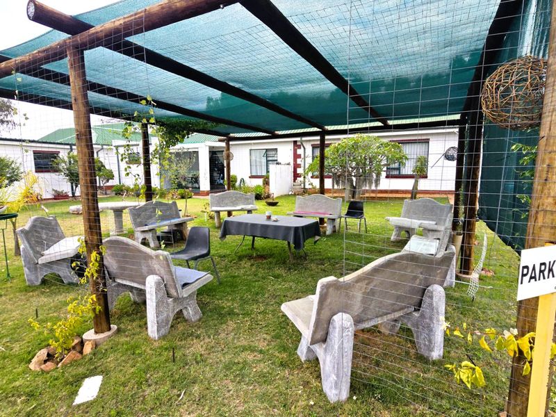 Outdoor entertainment area featuring a timber-framed shade netting structure and fixed concrete bench seating set within a garden space.