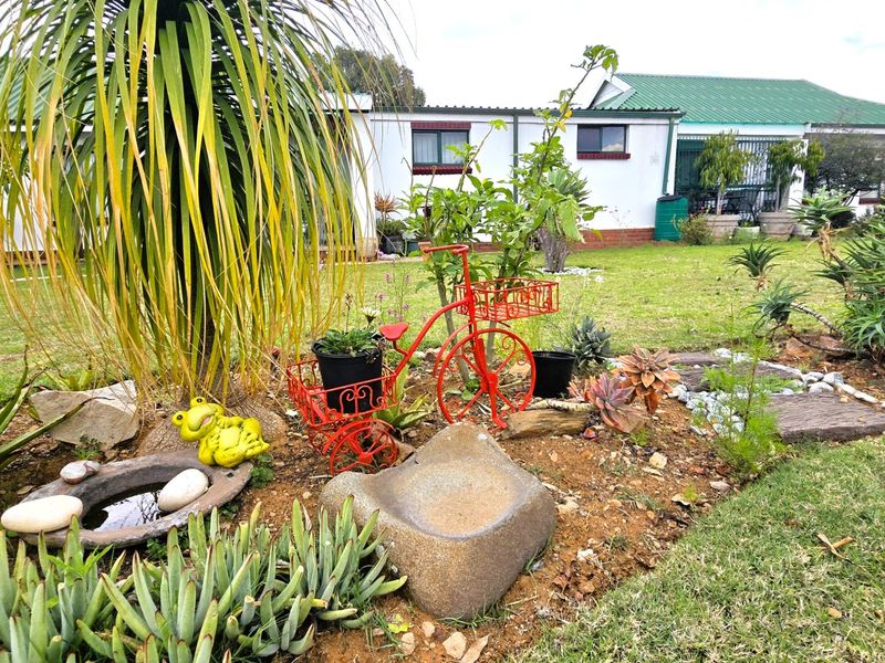 A view of the rear garden featuring a well-maintained lawn and established garden beds with a view of the townhouse exterior.
