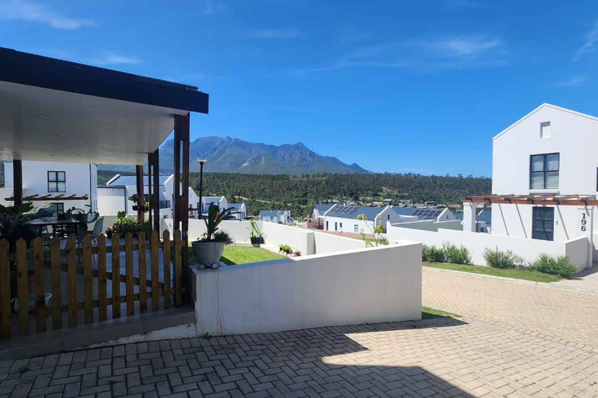 Front view of the property featuring a paved driveway, covered patio area, and scenic mountain views in a modern residential estate setting.
