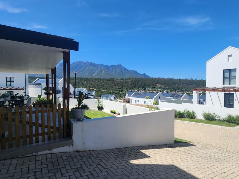 Front view of the property featuring a paved driveway, covered patio area, and scenic mountain views in a modern residential estate setting.