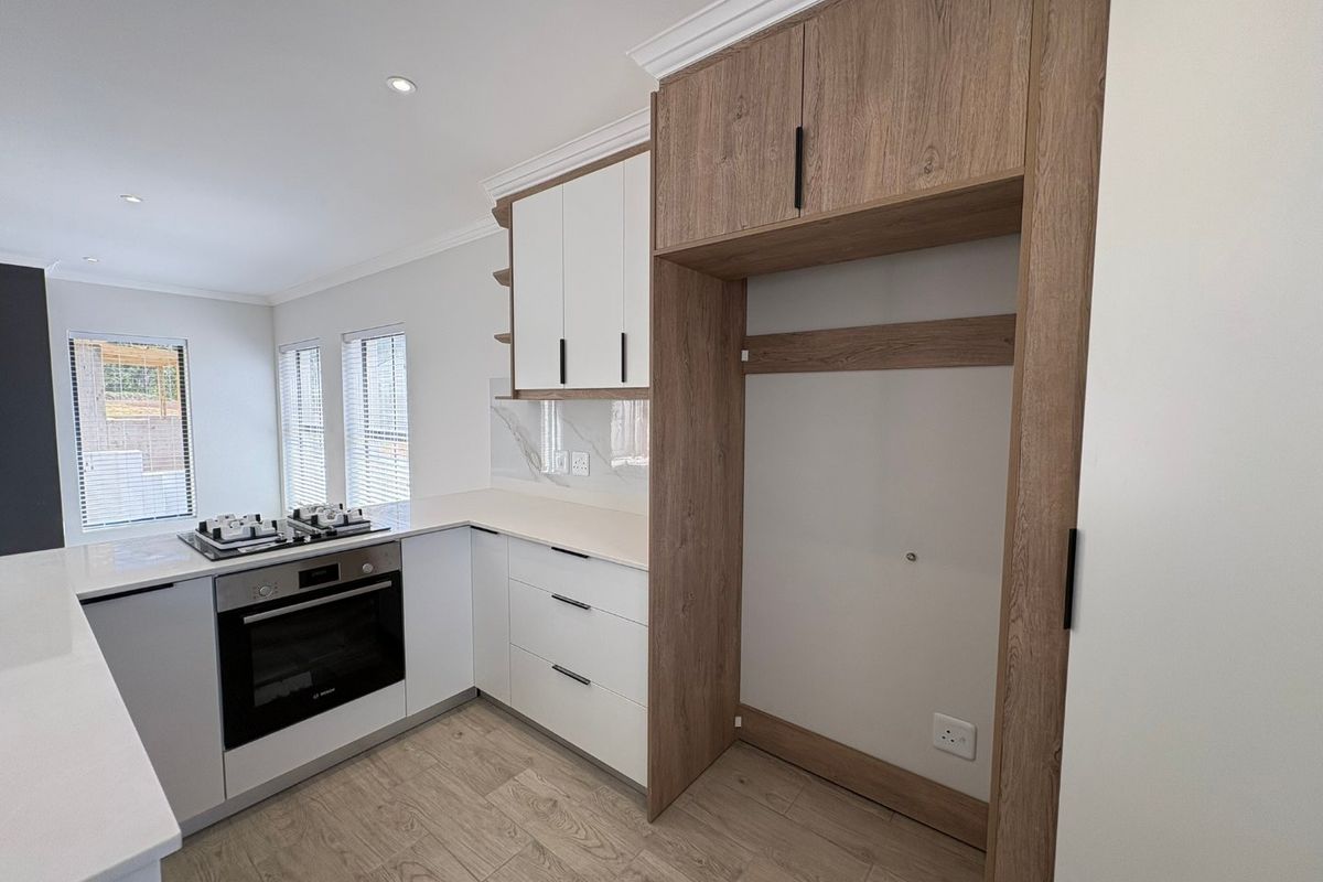Modern kitchen featuring sleek white and wood-tone cabinetry, stone countertops, built-in oven, gas hob, and high-quality tiled flooring in a bright, open space.