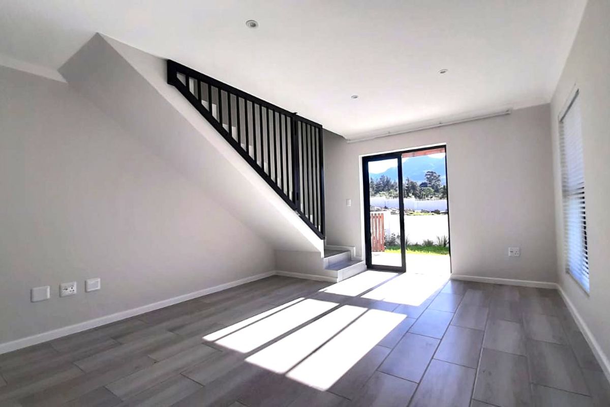 A bright, modern, and empty living room featuring tiled floors, a sleek black staircase balustrade, and a sliding glass door leading to the outdoors.