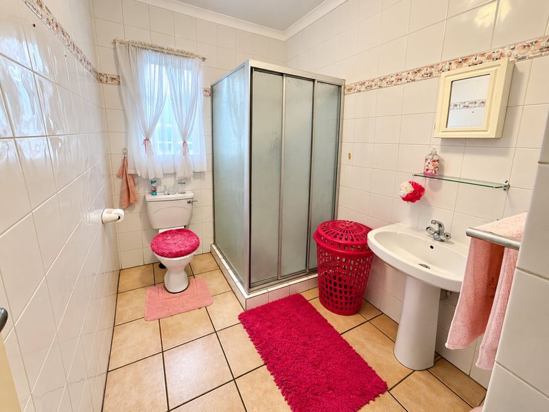 A functional bathroom featuring a shower enclosure, pedestal basin, and toilet with neutral wall tiling and floor tiles.