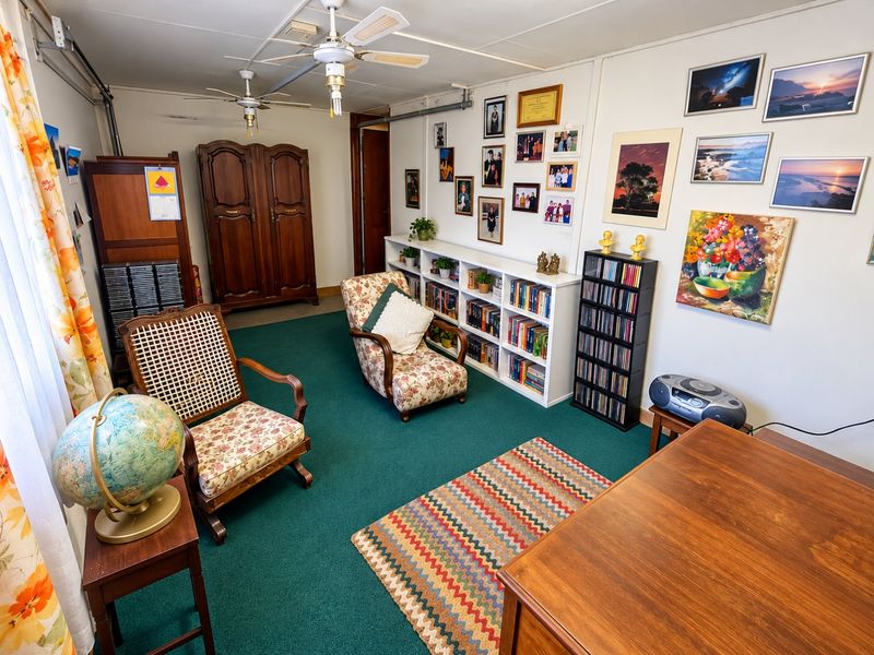 A living room featuring green carpeting, dual ceiling fans, and built-in shelving units, offering a functional space with potential for modernization.