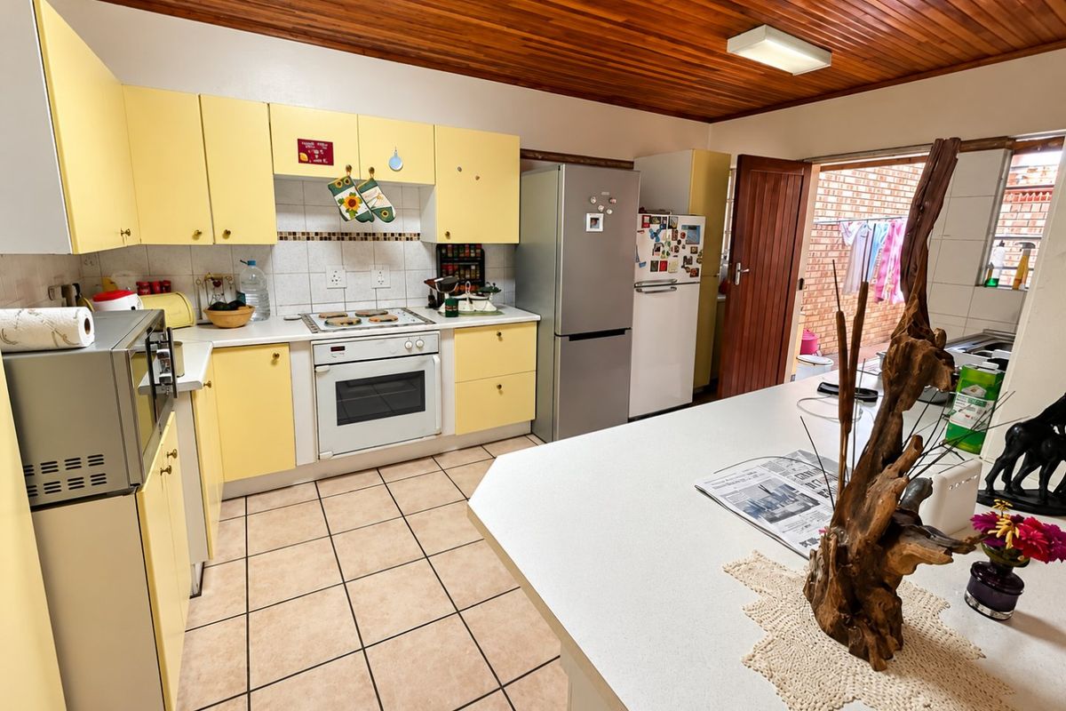 A functional kitchen featuring yellow cabinetry, tiled flooring, a timber ceiling, and a central island, with direct access to an outdoor area.