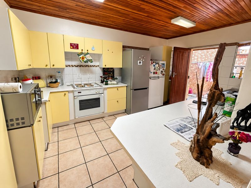 A functional kitchen featuring yellow cabinetry, tiled flooring, a timber ceiling, and a central island, with direct access to an outdoor area.
