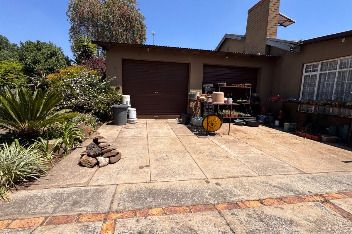 Rear exterior view of the property featuring a double garage, concrete driveway, and established garden area with brick-bordered paving.