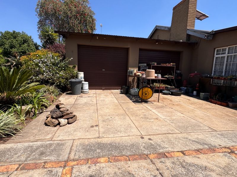 Rear exterior view of the property featuring a double garage, concrete driveway, and established garden area with brick-bordered paving.