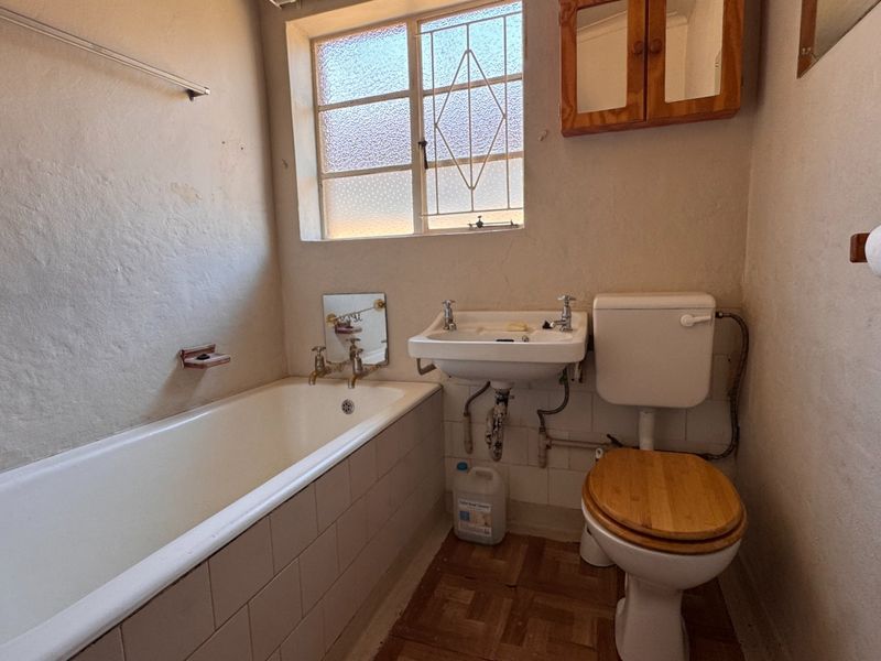 A dated bathroom featuring a standard bathtub, wall-mounted basin, and toilet, requiring modernization of finishes and fixtures to improve functionality and aesthetic appeal.