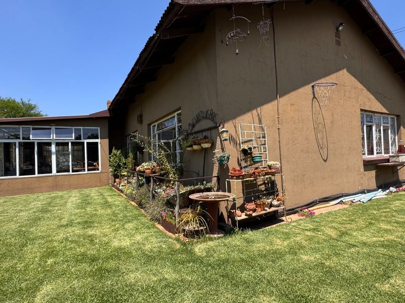 Rear view of the property featuring a lawn, enclosed patio area, and plastered exterior walls with security window bars.