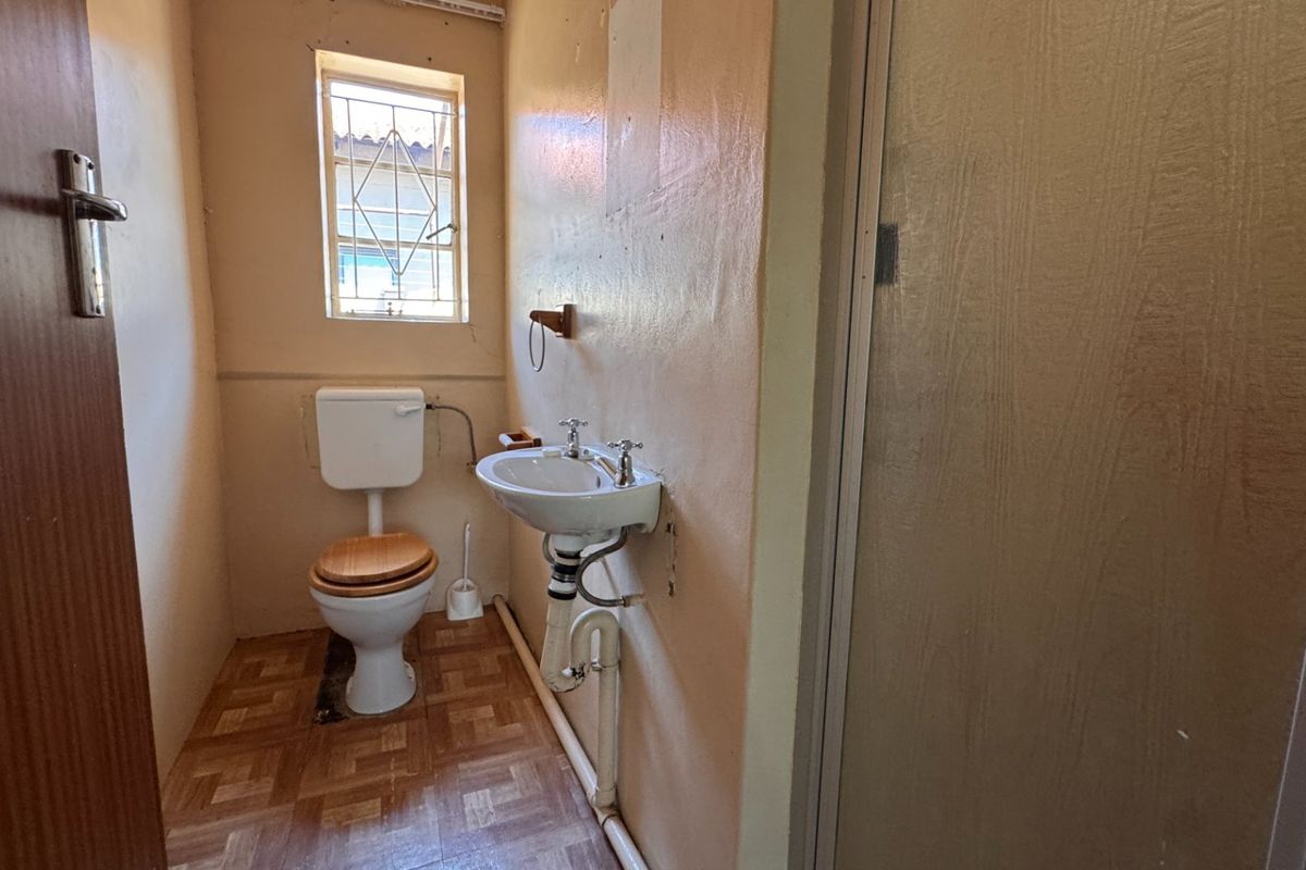 A compact bathroom featuring a wall-mounted basin, toilet, and shower enclosure, requiring cosmetic updates to modernize the dated finishes and exposed plumbing.