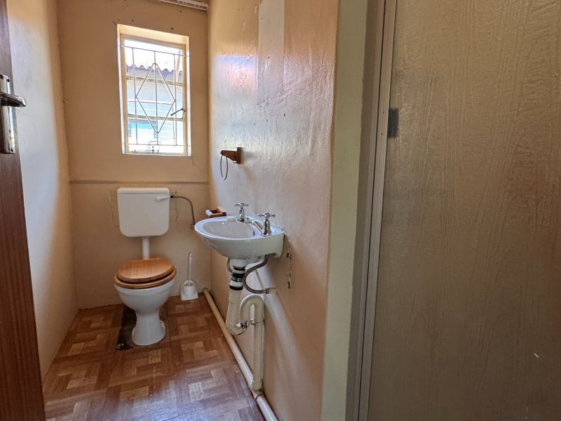 A compact bathroom featuring a wall-mounted basin, toilet, and shower enclosure, requiring cosmetic updates to modernize the dated finishes and exposed plumbing.