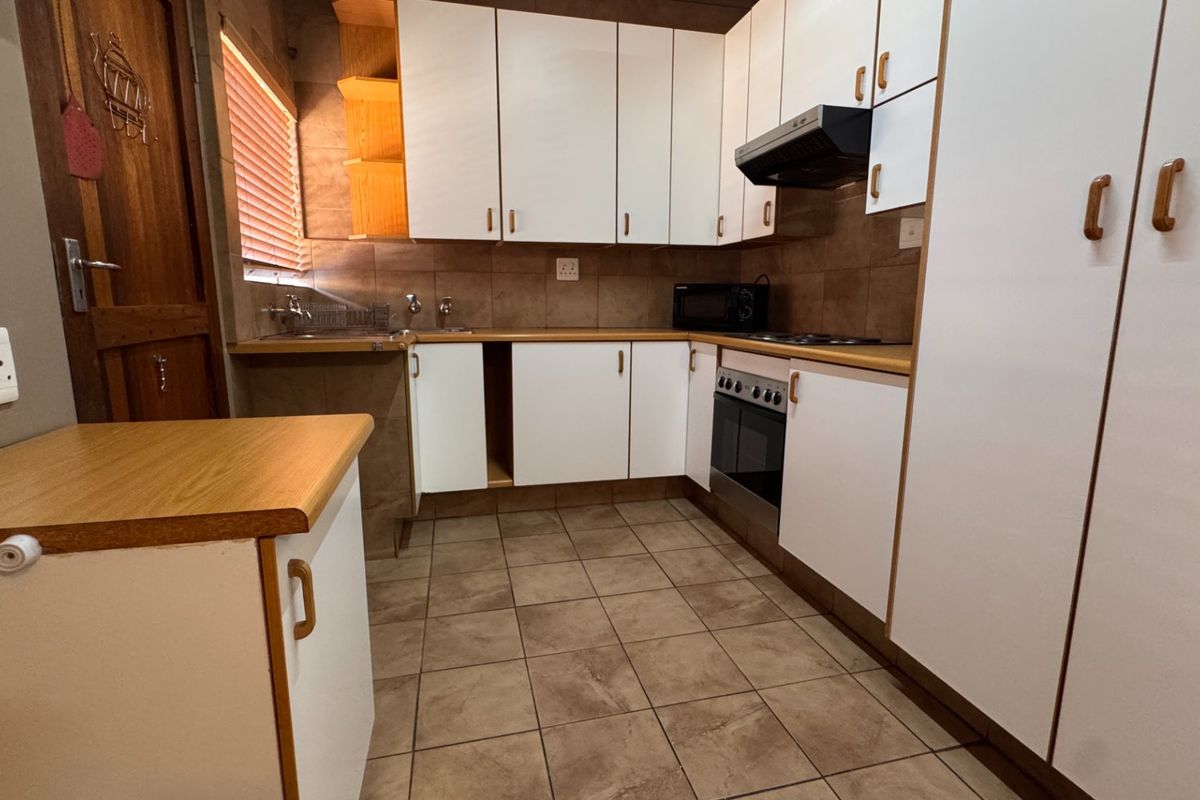 A functional kitchen featuring white cabinetry, laminate countertops, tiled backsplash, and built-in cooking appliances, requiring minor repairs to cabinetry.