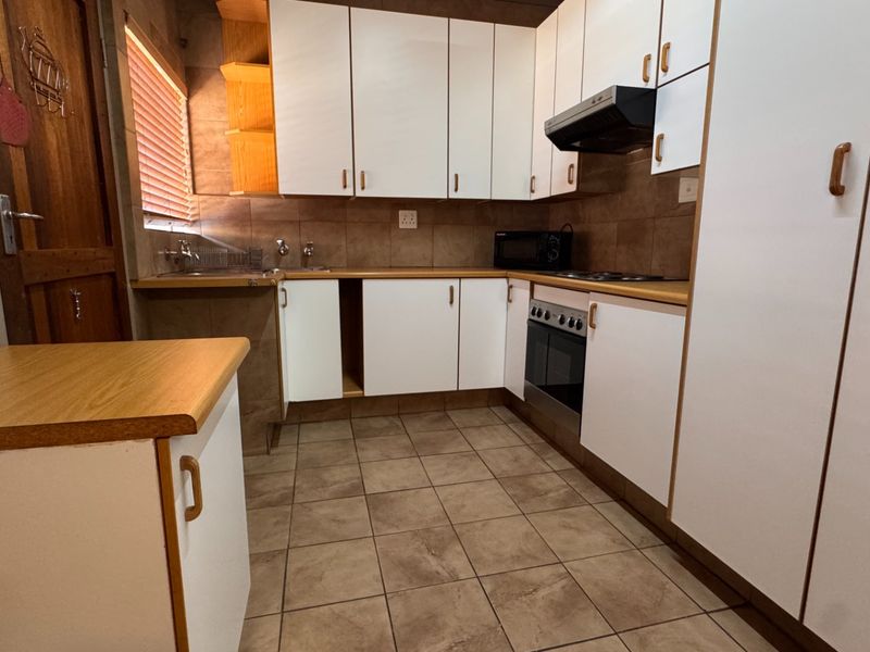 A functional kitchen featuring white cabinetry, laminate countertops, tiled backsplash, and built-in cooking appliances, requiring minor repairs to cabinetry.