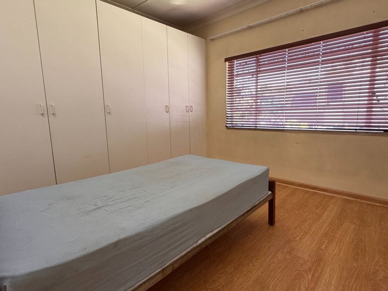 A bedroom featuring laminate flooring, built-in cupboards, and venetian blinds. The room offers a functional layout with neutral finishes.