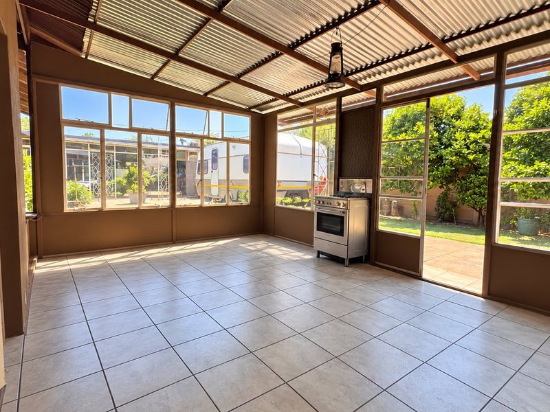 A spacious, light-filled enclosed patio featuring tiled flooring, a corrugated roof, and a freestanding gas stove, offering direct access to the garden.