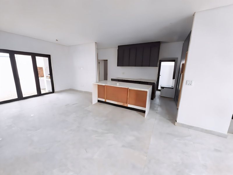 An open-plan living and kitchen area featuring tiled floors, a central island with stone countertop, and dark cabinetry, currently awaiting final finishing touches.