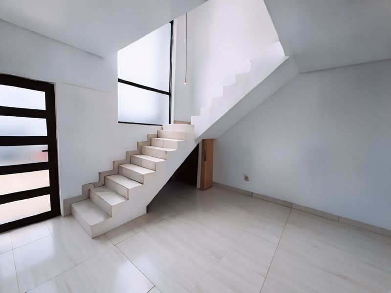 A bright, modern entrance area featuring clean tiled flooring, a minimalist staircase, and built-in under-stair storage, offering a spacious and contemporary feel.