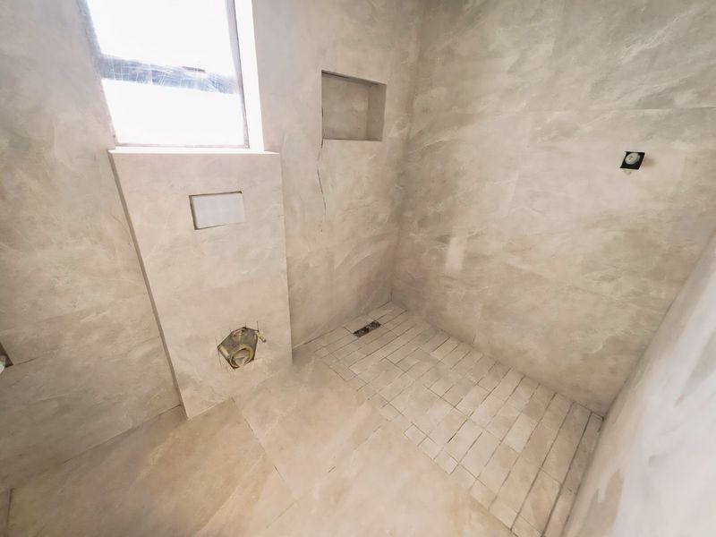 An unfinished bathroom space featuring tiled walls, a recessed niche, and a walk-in shower area with a linear drain, currently awaiting final fixtures.