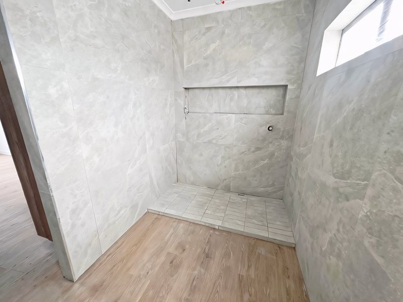 A modern, unfinished walk-in shower area featuring large-format marble-look wall tiles, a built-in recessed niche, and wood-look flooring.
