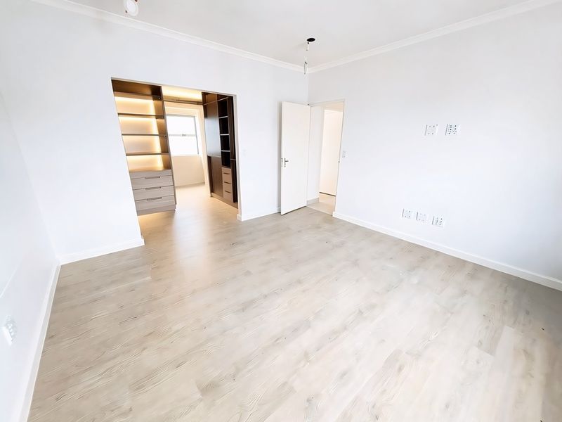 A bright, empty bedroom featuring modern laminate flooring, built-in cupboards with integrated lighting, and a clean, neutral finish throughout.