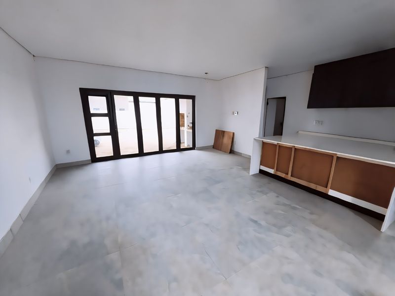 Spacious open-plan living and kitchen area featuring large glass sliding doors, tiled flooring, and an unfinished kitchen island with an extractor hood.