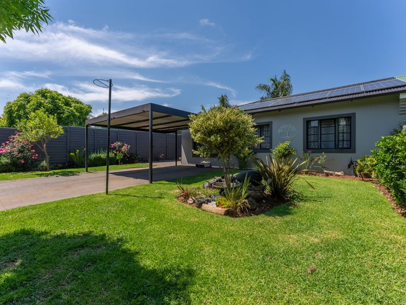 A well-maintained front exterior featuring a paved driveway, a modern carport, solar panels on the roof, and a landscaped garden.