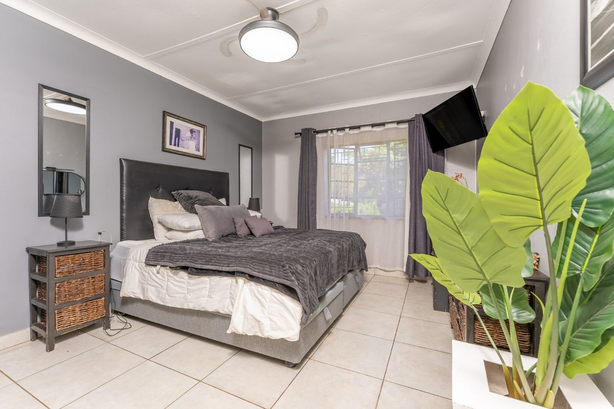 A functional bedroom featuring tiled flooring, a ceiling fan, and neutral grey walls, offering a comfortable and practical living space.