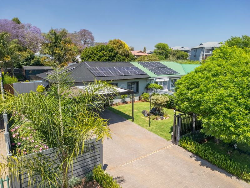 Aerial view of the front elevation featuring a paved driveway, carport, and roof-mounted solar panels set within a landscaped garden.