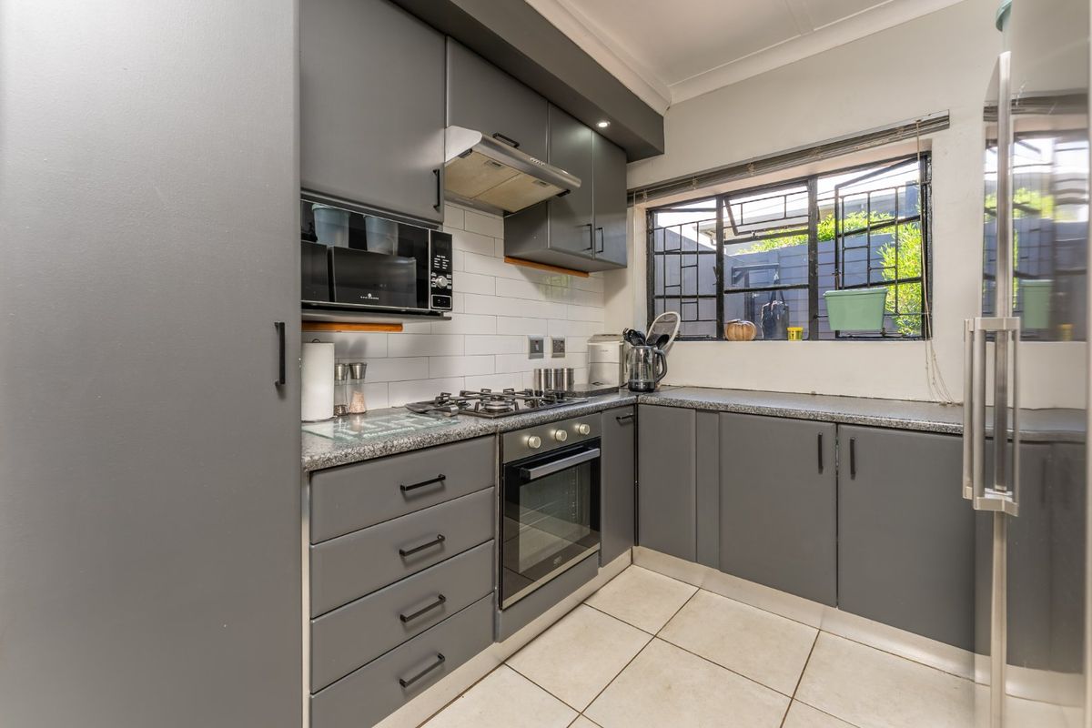 Modern kitchen featuring grey cabinetry, granite countertops, gas hob, built-in oven, and subway tile backsplash with natural light from the window.