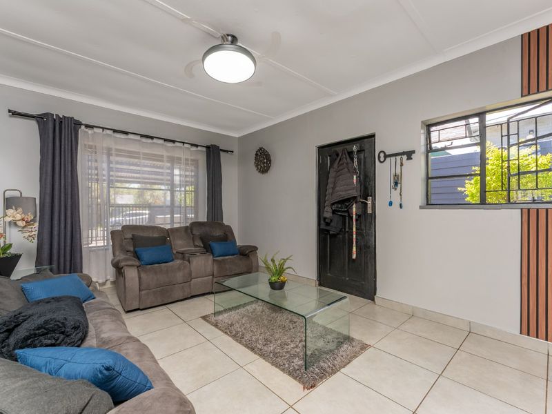 A well-maintained living room featuring tiled flooring, a ceiling fan, and a decorative wood slat accent wall.