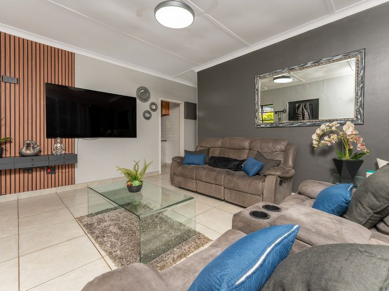 A modern living room featuring a slatted wood accent wall, neutral tiled flooring, and a contemporary ceiling light fixture.