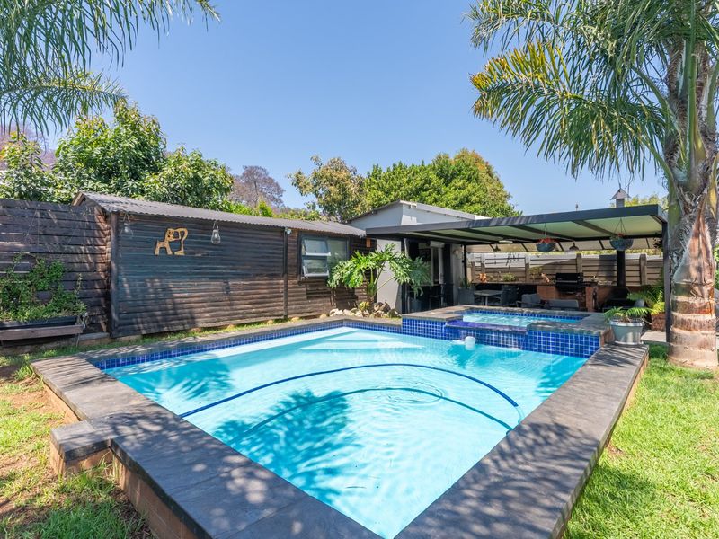 Outdoor entertainment area featuring a swimming pool with integrated spa, adjacent covered patio with built-in braai, and landscaped garden surroundings.