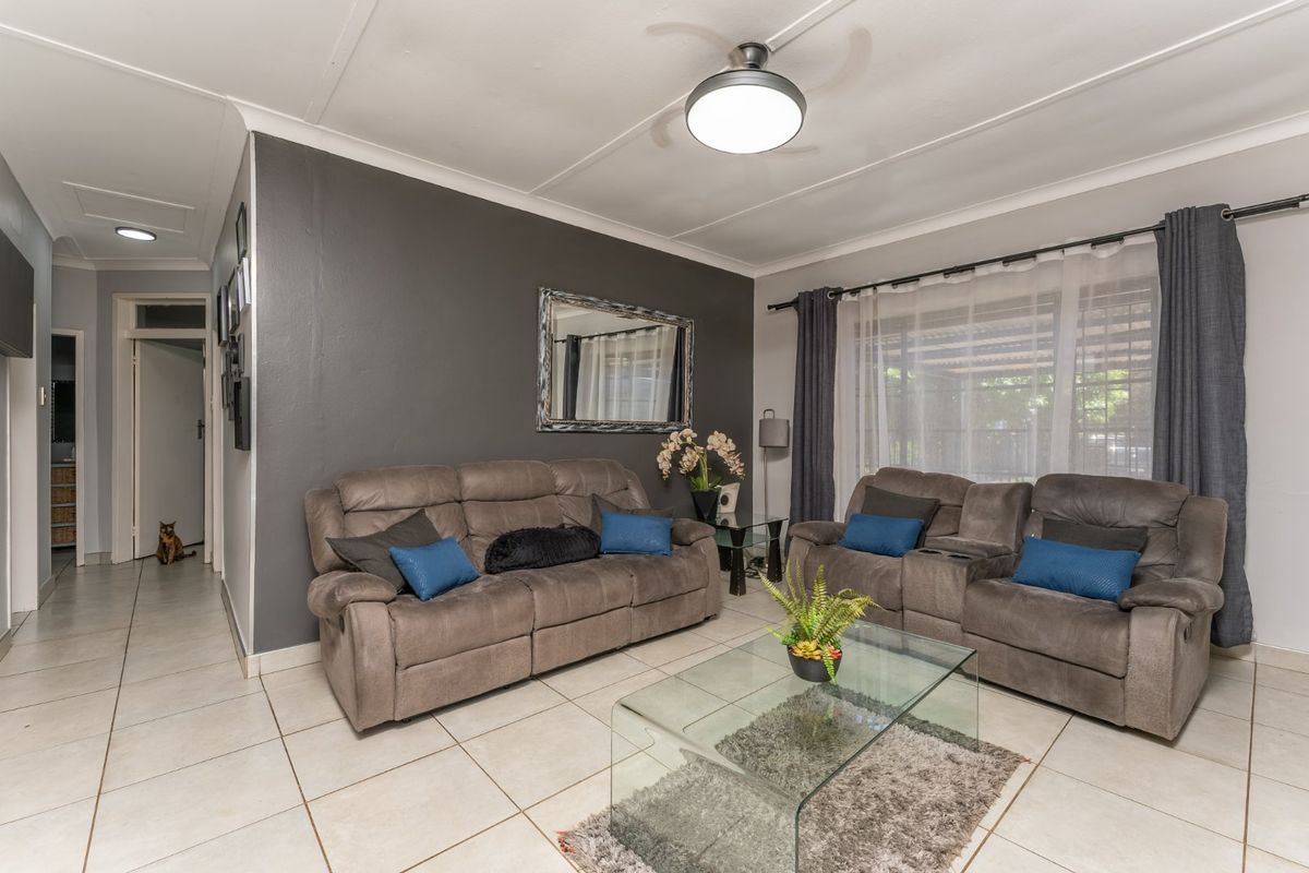 A well-maintained living room featuring neutral tiled flooring, a central ceiling fan, and a dark accent wall.
