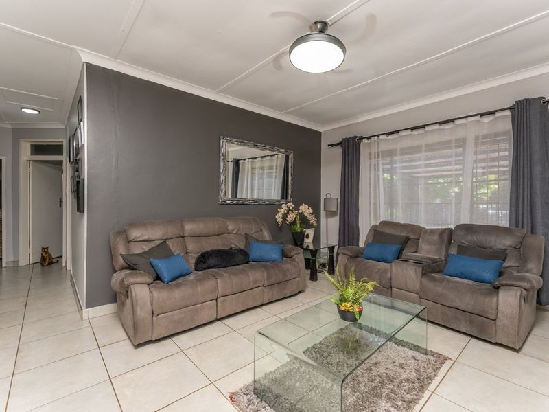 A well-maintained living room featuring neutral tiled flooring, a central ceiling fan, and a dark accent wall.