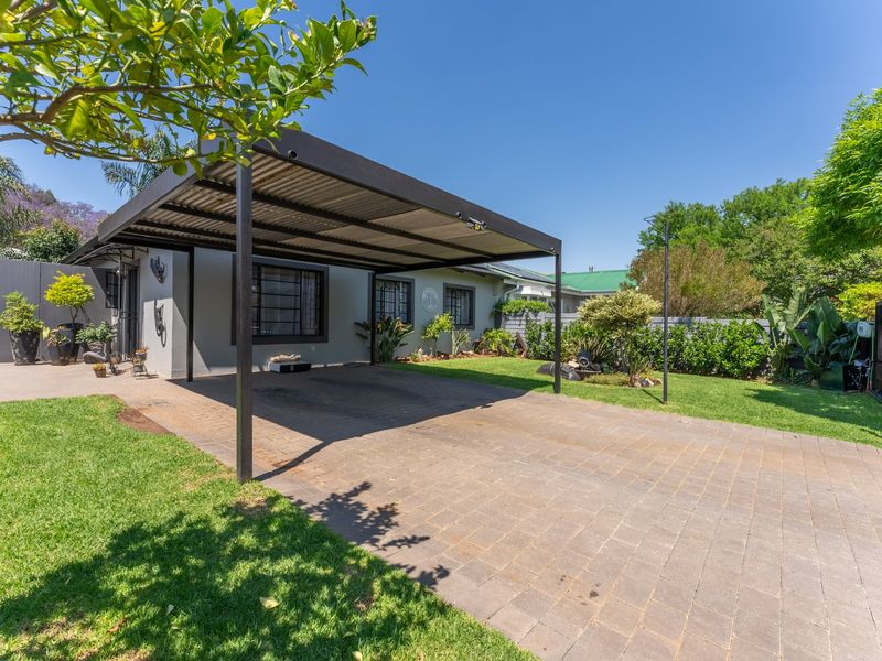 A well-maintained front exterior featuring a modern metal carport, paved driveway, and a neatly landscaped garden with secure boundary walls.