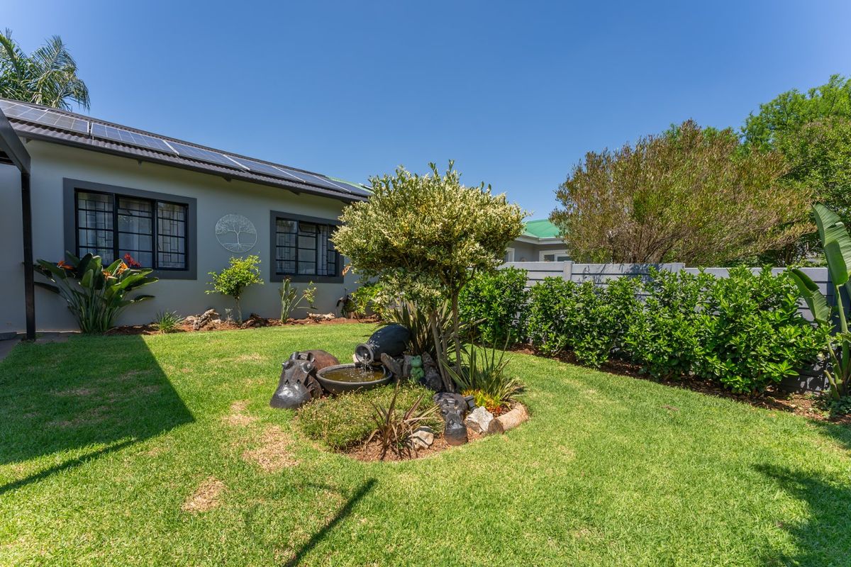 A well-maintained rear garden featuring a landscaped lawn, established shrubbery, a decorative water feature, and solar panels installed on the roof.